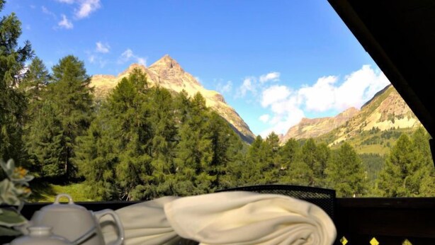 Taula posta amb plats blancs i una tovalla, amb vista a un paisatge de muntanya amb boscos densos.