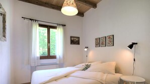 Un dormitori amb un llit, una taula de nit, una làmpada, una finestra amb cortines i un penjant de sostre.