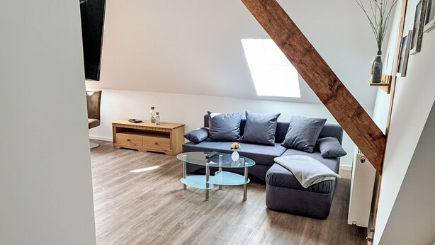 Un soggiorno moderno con tavolino in vetro, divano grigio, credenza in legno e soffitto spiovente.