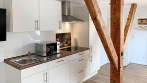 Una cucina moderna con mobili bianchi, un lavello in acciaio inossidabile e un forno a microonde. In centro, una struttura con travi in legno.