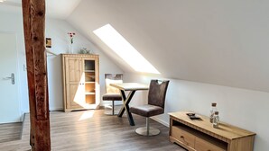 Una stanza in stile loft con soffitto spiovente, pavimento in legno, un tavolo da pranzo con sedie, un armadietto in legno e una piccola mensola in legno con bottiglie.