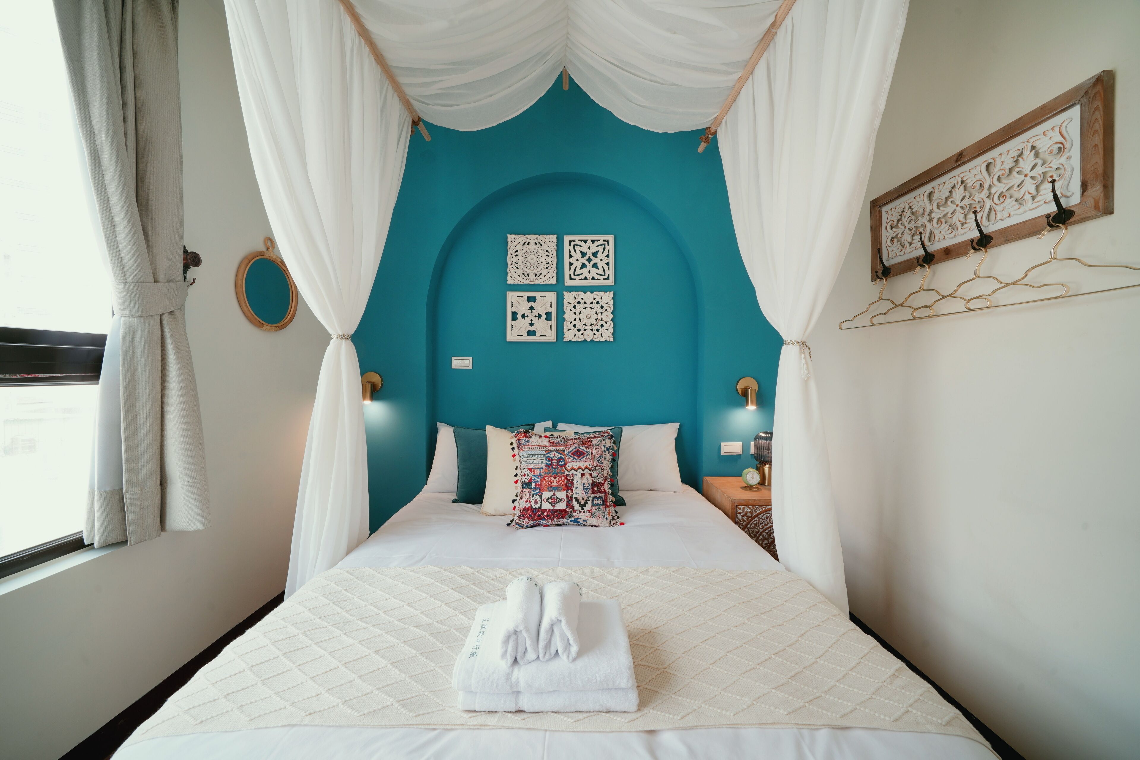 A bed with a white quilted bedspread, a neatly folded white towel, and a teal-colored headboard.