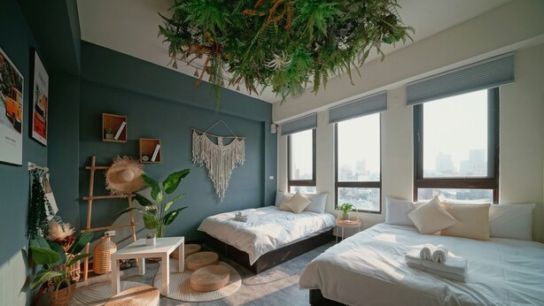 Une chambre moderne avec un grand lit, un plus petit lit, un bureau et une plante suspendue.