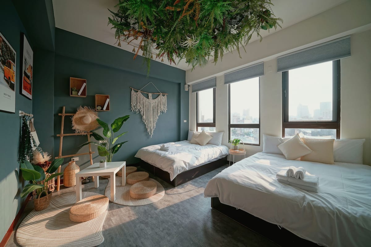 A modern bedroom with a large bed, a smaller bed, a desk, and a hanging plant.