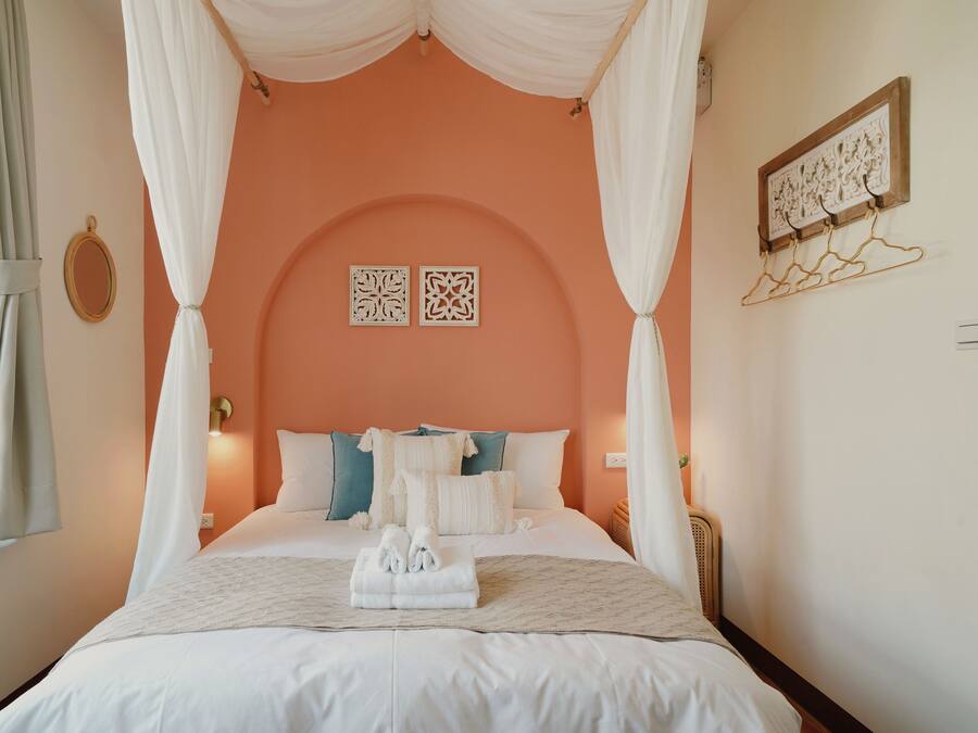 A bedroom with a four-poster canopy bed, white bedding, and a neatly folded towel on the bed.