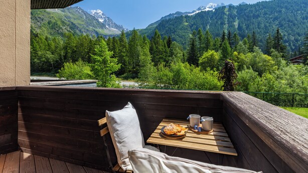 Una terraza de madera con una mesa, una silla y vistas a un paisaje montañoso.