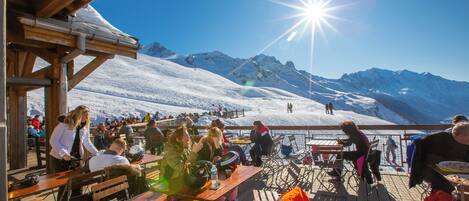 Une terrasse en bois, agrémentée de tables et de chaises, qui offre une vue sur un paysage montagneux enneigé.