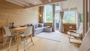 Un interior de madera con una mesa de comedor, sillas, un sofá y un ventanal con vistas al verdor.
