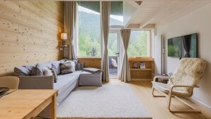 Una sala de estar moderna con una pared de madera, un sofá, un sillón, un televisor y vistas al verdor.