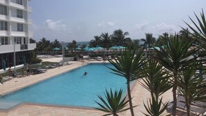 Une piscine entourée de palmiers et d’un bâtiment, avec des chaises longues et des parasols.