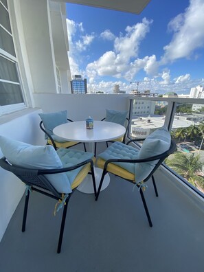 A balcony with a round table and four chairs, overlooking a cityscape with buildings and palm trees. - Beachfront apartment with Ocean View (Miami Beach)