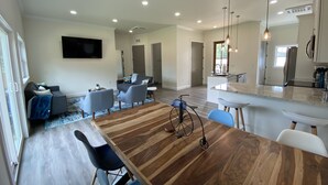 A modern open-plan living and dining area with a wooden dining table, blue chairs, a grey sofa, and a kitchen with a large island and pendant lighting. - Have the Best of Both: Quick Access to Downtown Brevard & Pisgah Forest. (Brevard)