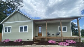 A two-story house with a porch, a front door, and a small garden with pink flowers. - Have the Best of Both: Quick Access to Downtown Brevard & Pisgah Forest. (Brevard)