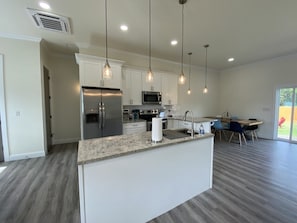 A modern kitchen with white cabinets, stainless steel appliances, and pendant lighting.