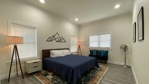 A bedroom with a bed, bedside tables, a floor lamp, a standing fan, and a decorative wall piece. - Have the Best of Both: Quick Access to Downtown Brevard & Pisgah Forest. (Brevard)