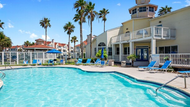 A swimming pool with lounge chairs and a building with a balcony. - Island Oasis! 1st floor! One block to the beach! (Corpus Christi)