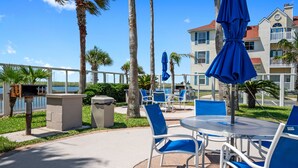 An outdoor patio with blue chairs and umbrellas, a grill, and a view of the water and buildings. - Island Oasis! 1st floor! One block to the beach! (Corpus Christi)