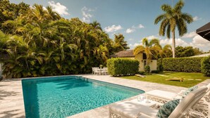 A swimming pool with a tiled deck, surrounded by lush greenery and palm trees. - Modern home w/heated pool, BBQ & casita (West Palm Beach)