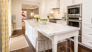 A modern kitchen with white cabinetry, a central island, stainless steel appliances, and a decorative flamingo wall art piece. - Modern home w/heated pool, BBQ & casita (West Palm Beach)