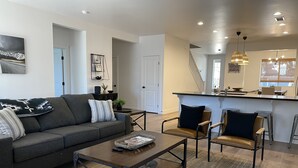 A modern living room with a sofa, coffee table, and chairs, a kitchen with a bar, and a staircase. - 5 Bedroom, 5 Minutes from Downtown (Flagstaff)