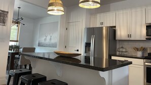A modern kitchen with white cabinets, a stainless steel refrigerator, and two pendant lights. - 5 Bedroom, 5 Minutes from Downtown (Flagstaff)