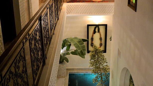 Una escala amb barana ornamentada, zona de piscina amb una planta en test i vista de la piscina des del nivell superior.