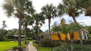 A pathway leading to a yellow building surrounded by palm trees and well-maintained greenery. - ✪KING BED LARGE VILLA✪ Close to Disney & Outlets! (Kissimmee)