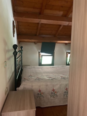 A bedroom with a wooden ceiling, a bed with a floral bedspread, a nightstand, and a window with a view of the outside. - Beautiful and Quiet Villa In Residence In The Po Delta Oasis (Porto Levante)