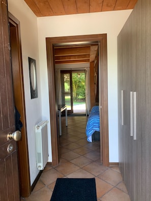 A hallway leading to a bedroom with a bed, a radiator, and a door with a handle.