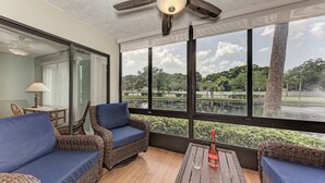 Ein Zimmer mit Korbmöbeln, einem Deckenventilator und Blick auf einen Park und See.