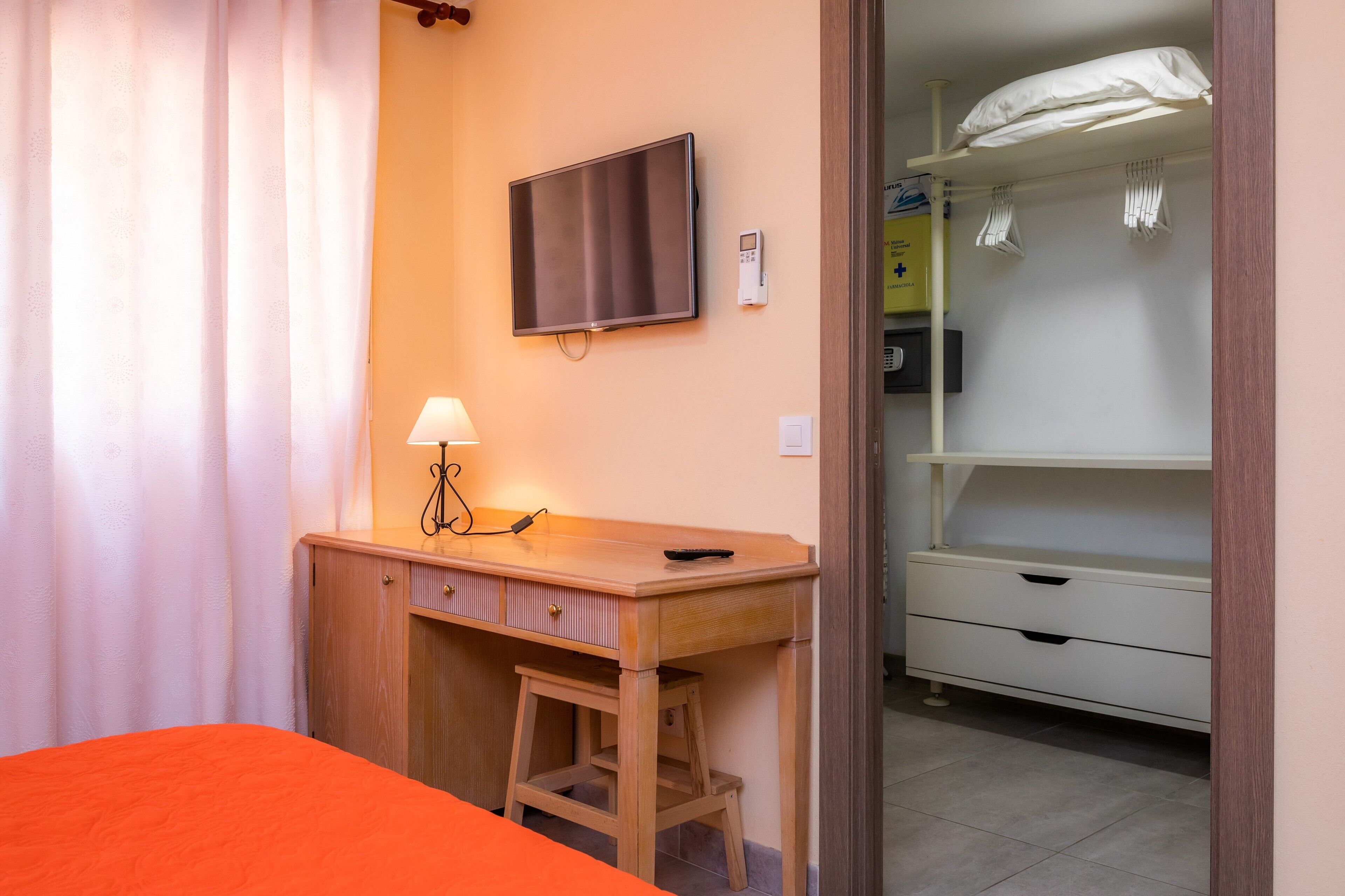 A hotel room with a bed, a desk with a lamp, a television, and a wardrobe.