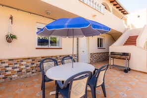 A patio with a round table, four chairs, a blue umbrella, a hanging plant, a grill, and a staircase. - "Can Caragol" Holiday Apartment with Private Terrace, A/C & WiFi (Cala Rajada)