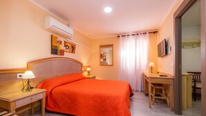 A hotel room with a bed, bedside table with a lamp, a desk with a chair, a TV, and a window with curtains. - "Can Caragol" Holiday Apartment with Private Terrace, A/C & WiFi (Cala Rajada)