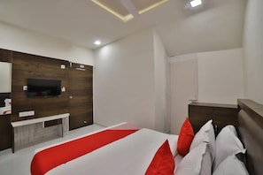 A modern hotel room with a large bed, a wooden accent wall, a flat-screen TV, and a small desk with a chair. - Hotel Maan Palace (Ahmedabad)
