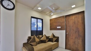 A room with a sofa, a wooden door, a ceiling fan, and a window with blinds. - Hotel Maan Palace (Ahmedabad)