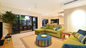 Un salon moderne avec un canapé vert, un pouf bleu et une grande plante en pot.