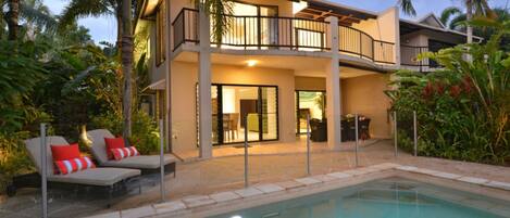 A two-story house with a balcony, a swimming pool, and outdoor furniture.