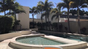 A swimming pool with a surrounding deck, palm trees, and a building in the background.