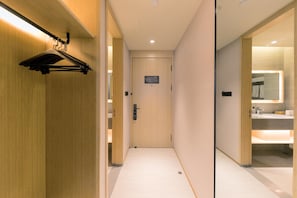 A hotel corridor with a wooden door, a coat rack, and a bathroom with a mirror and sink. - Ji Hotel (Shanghai)