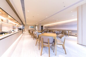 A modern dining area with wooden tables and chairs, a long counter with kitchenware, and a wall with a mountain landscape mural.