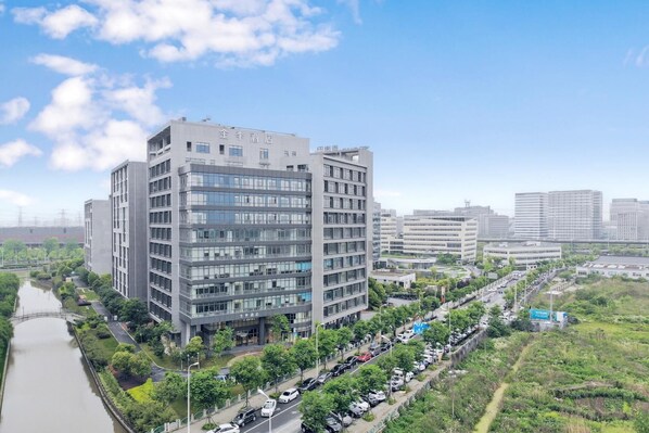 A modern multi-story hotel with a river in front, surrounded by greenery and other buildings. - Ji Hotel (Shanghai)