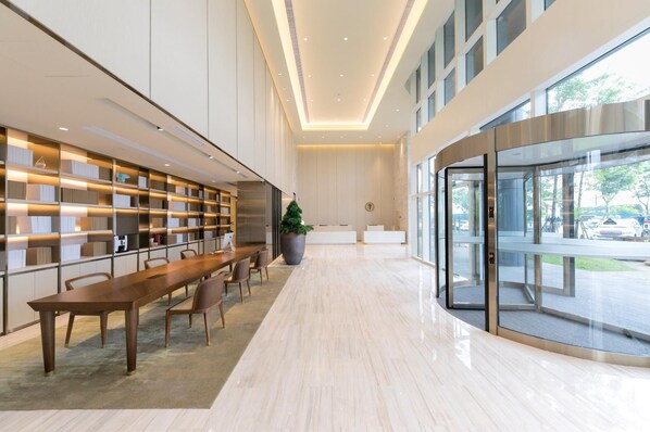 A modern library with a long wooden table, bookshelves, and a large potted plant.