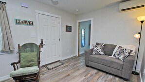 A living room with a rocking chair, a grey sofa, and a door leading to another room.