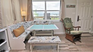 A cozy room with a sofa, a small table, a rocking chair, and a view of the sea through a window.