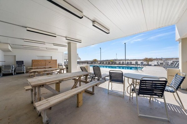Un patio al aire libre con mesas y sillas de picnic, una piscina al fondo y una vista despejada de la playa.