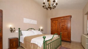A bedroom with a bed, a wooden wardrobe, a nightstand, a chandelier, and a radiator. - Casale Vittoria (Montopoli in Val d'Arno)