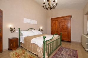 Quarto com cama, guarda-roupa de madeira, mesa de cabeceira, candelabro e radiador.