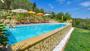 A swimming pool with lounge chairs and umbrellas, surrounded by greenery and a stone wall. - Casale Vittoria (Montopoli in Val d'Arno)