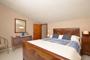 Quarto com cama de madeira, penteadeira, espelho e mesa de cabeceira.
