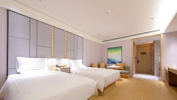 A hotel room with two beds, a sofa, a painting, and a door leading to a bathroom.
